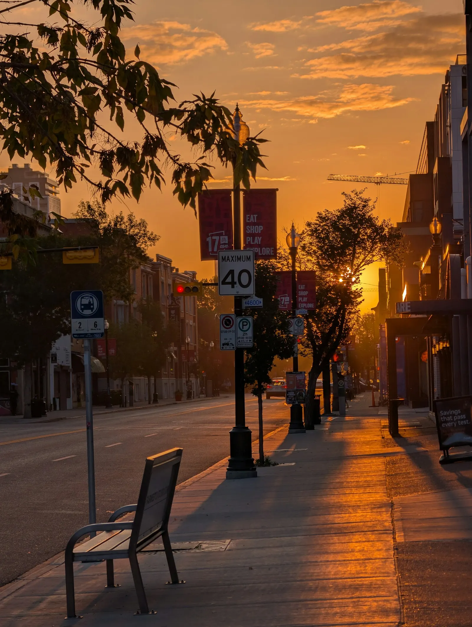 Empty street washed in orange light at sunrise, a bench on the pavement