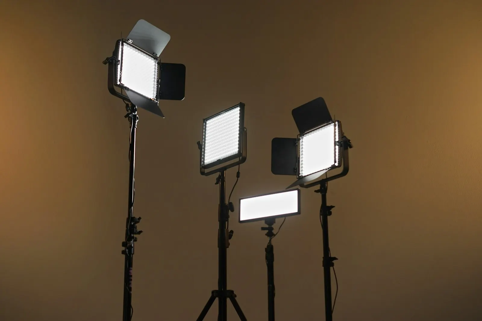 Four LED panels on stands with barn doors open against a brown wall