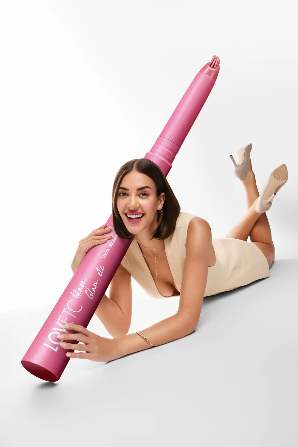 Model lying on the studio floor hugging an oversized pink LOVETC lip conditioner prop