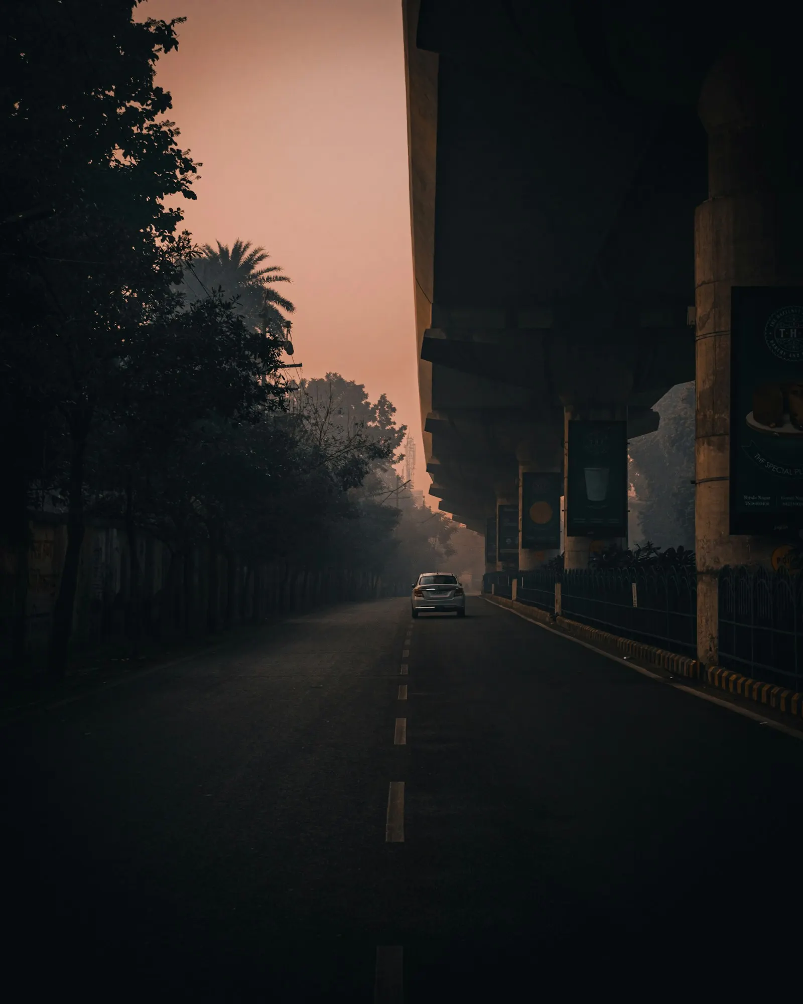 Empty road under a flyover at dawn with a single car approaching