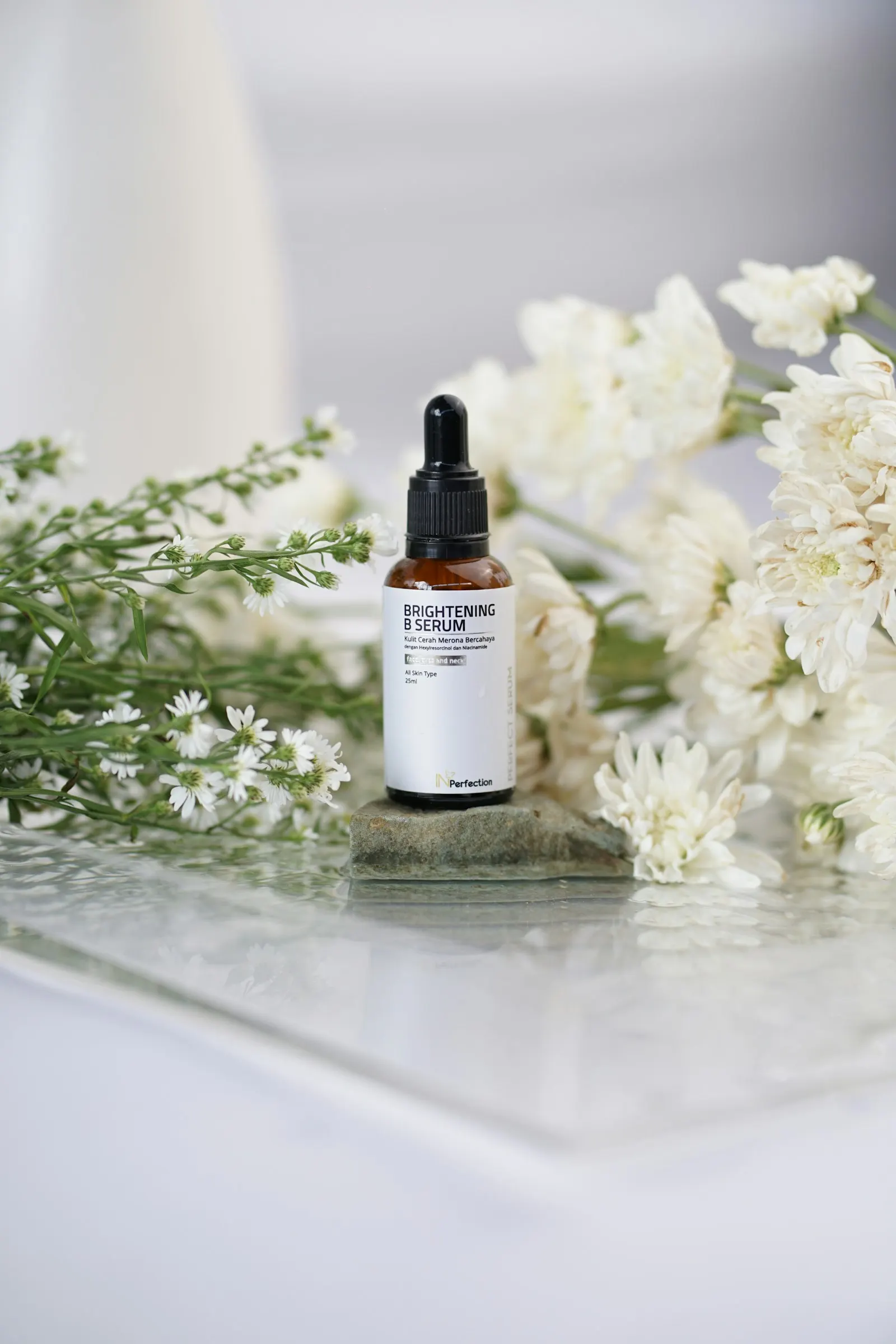 Serum bottle with a black dropper cap beside white flowers on glass