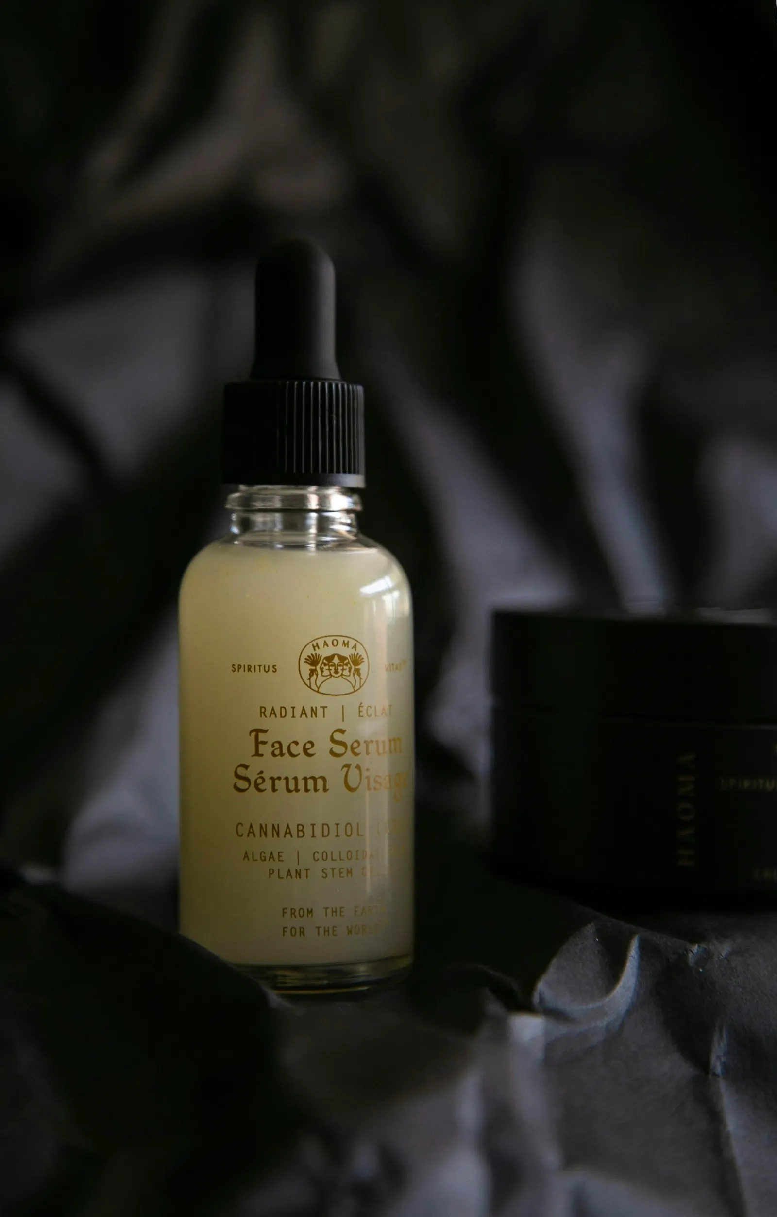 Face serum dropper bottle standing on dark fabric in low light