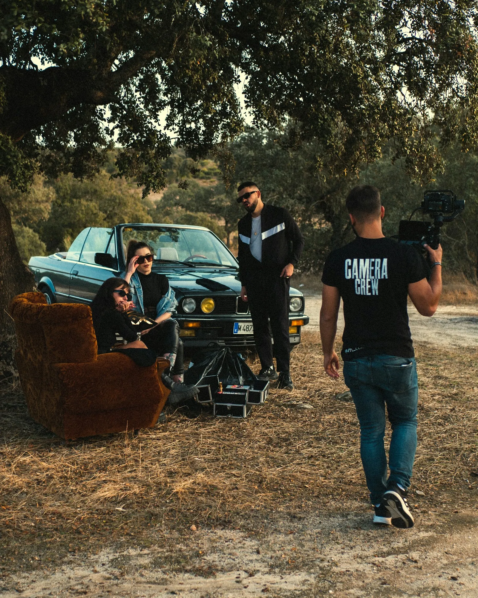 Camera operator carrying a gimbal towards an outdoor set with a vintage car